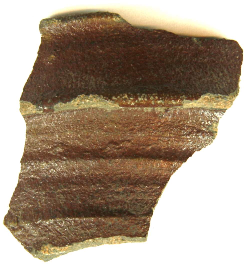 Randsk�r af gr�br�ndt n�sten stent�j fra kande/stob med bred, nedfaldende mundingsrandskrave. Yder- og indersiden er d�kket med manganbrunlig bemaling, hvorover klar slatglasur.