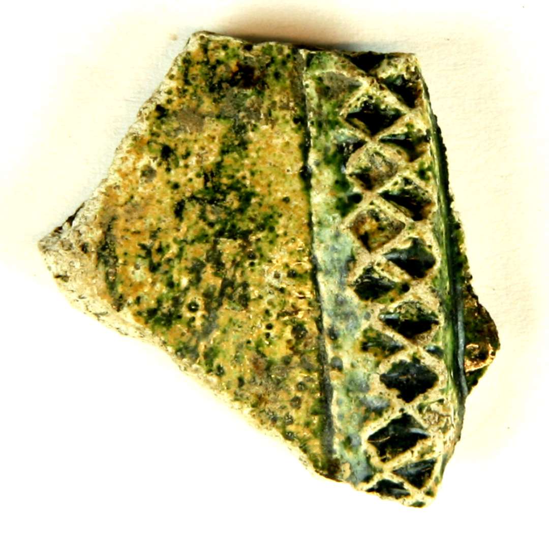 Bugsk�r af por�st pibelersagtigt gods fra kar, der p� ydersiden er forsynet med et p�lagt vulstb�nd med indstemplede rhombeformede fordybninger. Ydersiden og delvis indersiden er forsynet med gr�nligsp�ttet blyglasur.