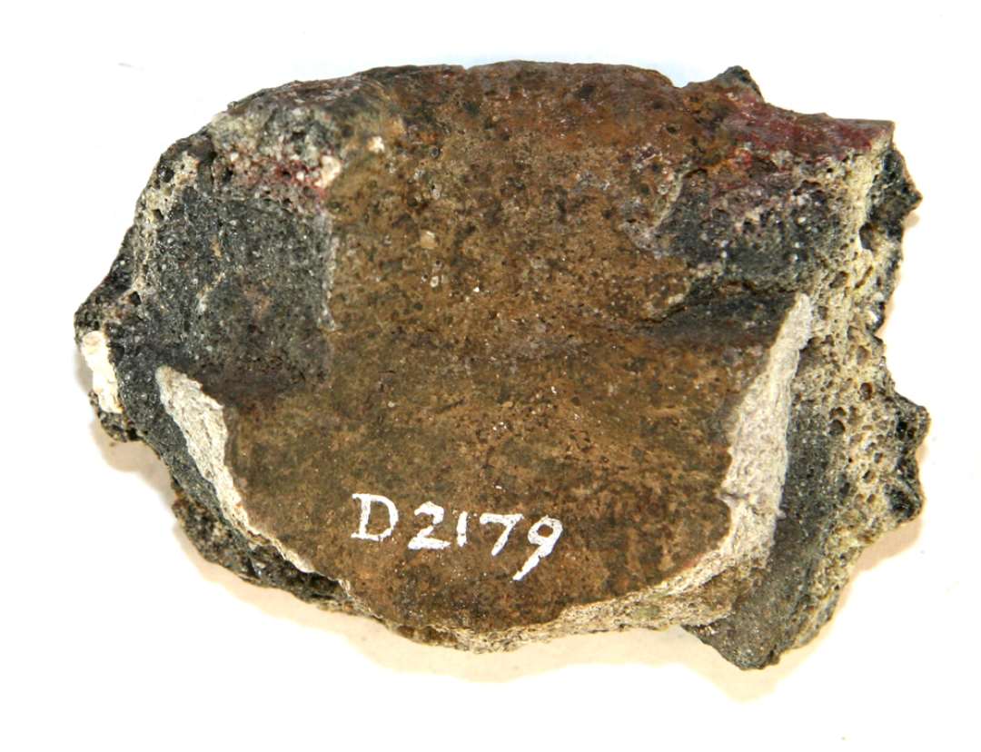 1 mundingsrandsk�r fra smeltedigel af gr�ligt, por�st, sandblandet gods, der p� ydersiden er d�kket af en sintret uj�vn lerkappe, hvis overflade fremtr�der som et r�dgr�t, glasuragtigt lag. Under skorpen ses en glat mundingsrand med skarp ydre rand og let indadskr�nende overkant.