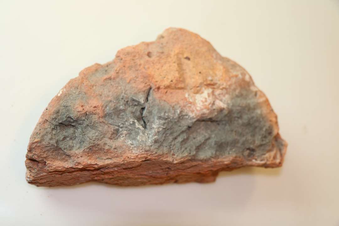 En halvrund munkesten med et indhak p� rundsiden. Der er indhakket et kors/grafitti p� undersiden.�M�l ca. 24 x 13 x 7 cm. 