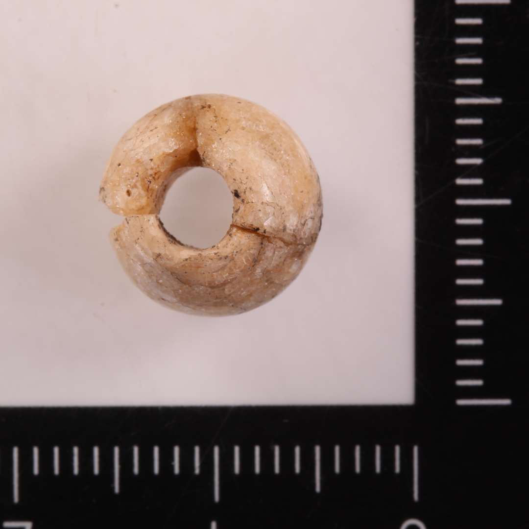 Glasperle nu af cremefarvet dekomponeret glas. Konisk facon. diameter: ca 1,1 cm. Let fragmenteret.