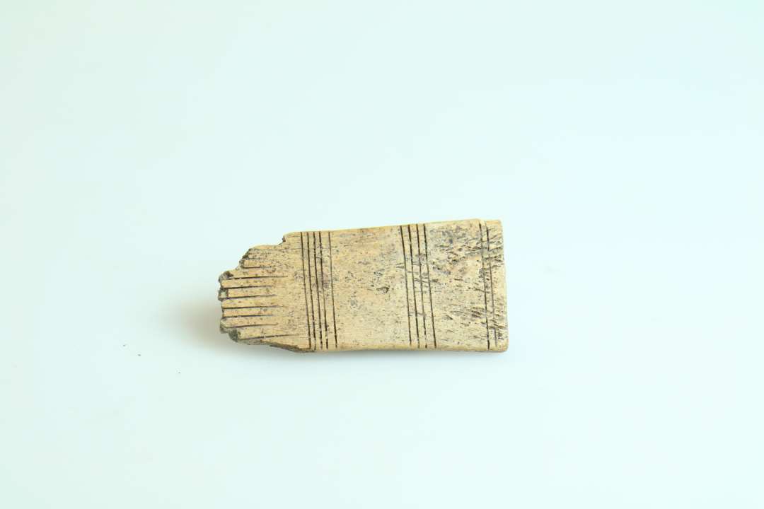 Fragment af langtandskam med stregornamentik, uden t�nder.�St�rste m�l ca. 6 cm.��P�nt tildannet langtandskam med dekoration p� begge sider af hovedet i form af tre grupper tv�rstreger. Har haft 11 t�nder.