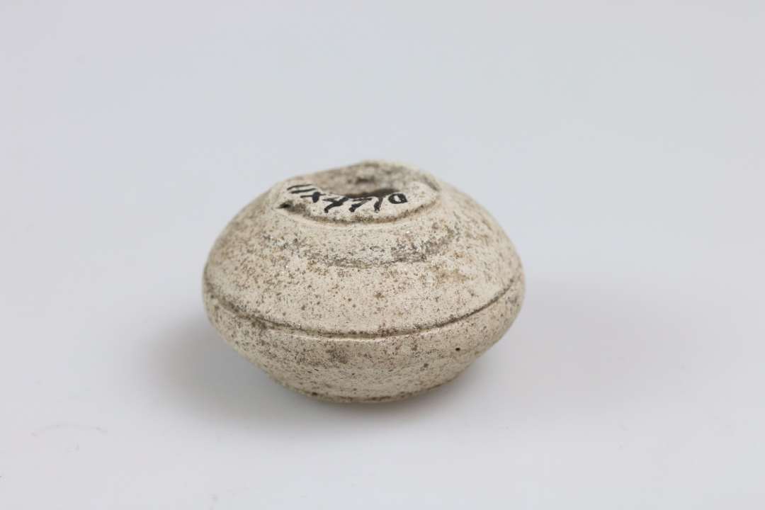 Stort set intakt, n�rmest dobbeltkonisk tenv�gt af hvidt ler med tre oml�bende streger. Diameter ca. 3 cm. Import.