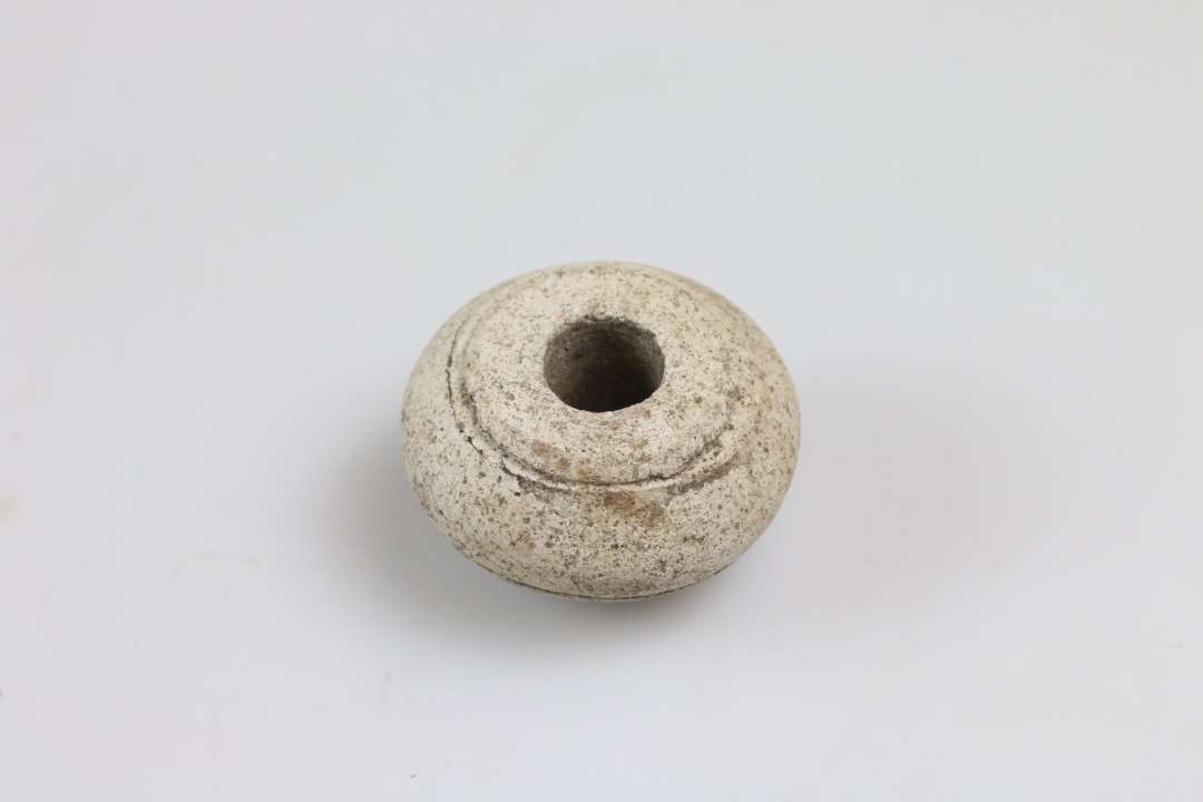 Stort set intakt, n�rmest dobbeltkonisk tenv�gt af hvidt ler med tre oml�bende streger. Diameter ca. 3 cm. Import.