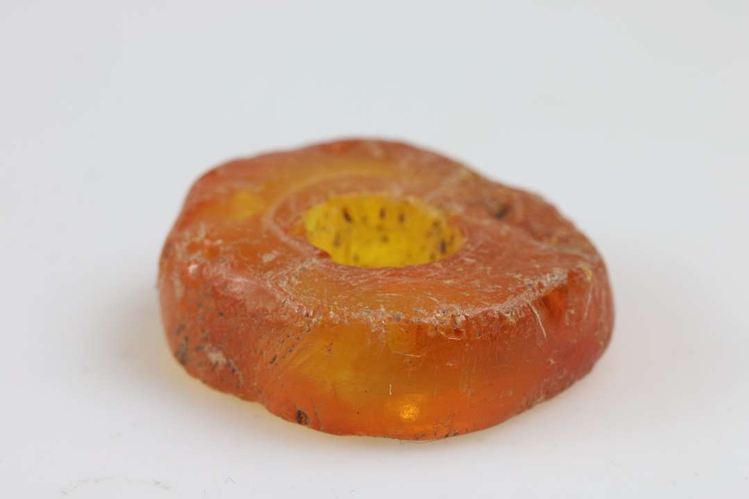 Stor ravperle eller anden genstand. Flad, skiveformet. tykkelse ca. 1 cm, diameter ca. 3 cm