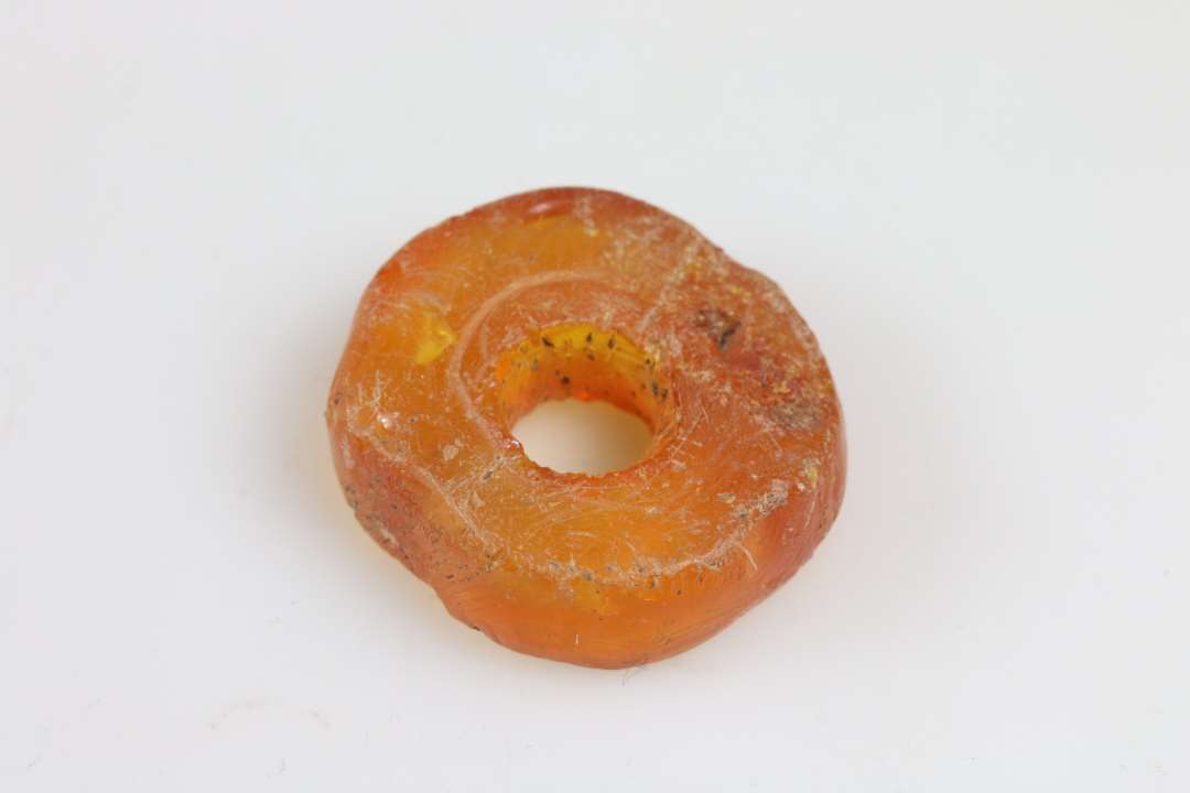 Stor ravperle eller anden genstand. Flad, skiveformet. tykkelse ca. 1 cm, diameter ca. 3 cm