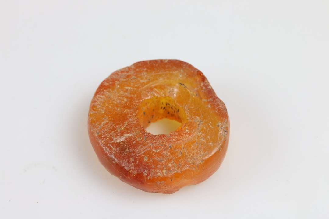 Stor ravperle eller anden genstand. Flad, skiveformet. tykkelse ca. 1 cm, diameter ca. 3 cm