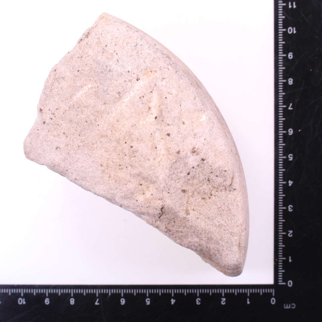 Fragment af cirkul�r, roterende slibesten. Der ses rester af den buede slibeflade samt den ene side, der er tilhugget med mejsel. M�l: 9x5,4x5,3 cm.