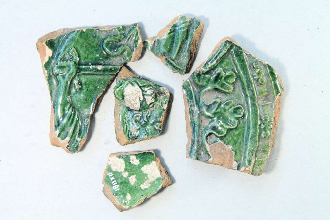 Fragmenter af gr�nglaserede kakler, bl.a. med kvindefigur (?) med sv�rd. M�ske motiv af Judith som dr�ber Holofernes, i stil med Donatellos statue i Firenze. Dette bibelmotiv var meget popul�rt p� ovnkakler, se s. 31-32 i 'Kakler' af Niels-Knud Liebgott (1972).