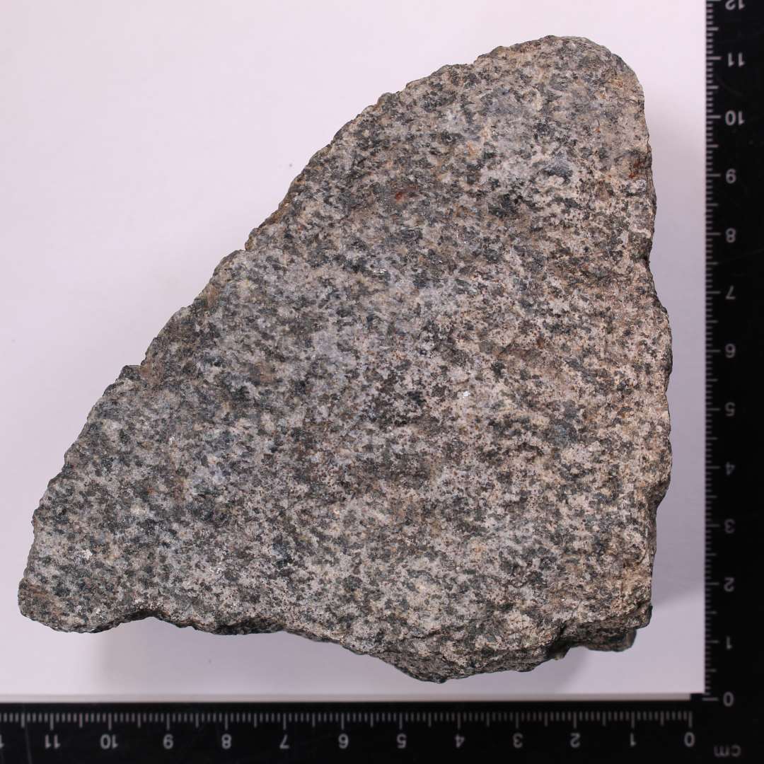 Fragment, granitsten med tydelig, behugget kant og ansats til cirkul�r form. Kv�rnstensfragment?