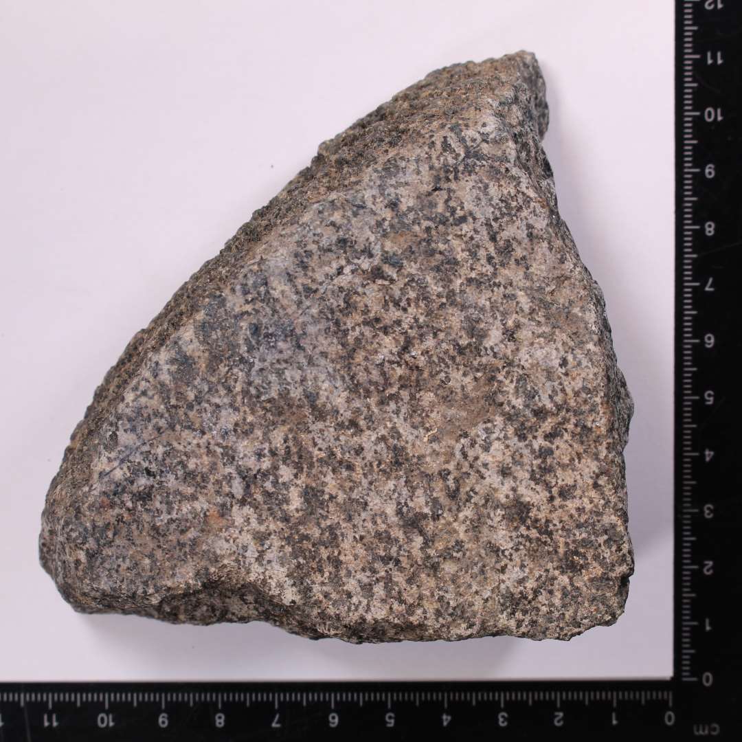 Fragment, granitsten med tydelig, behugget kant og ansats til cirkul�r form. Kv�rnstensfragment?