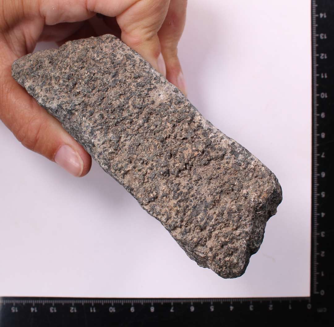 Fragment, granitsten med tydelig, behugget kant og ansats til cirkul�r form. Kv�rnstensfragment?