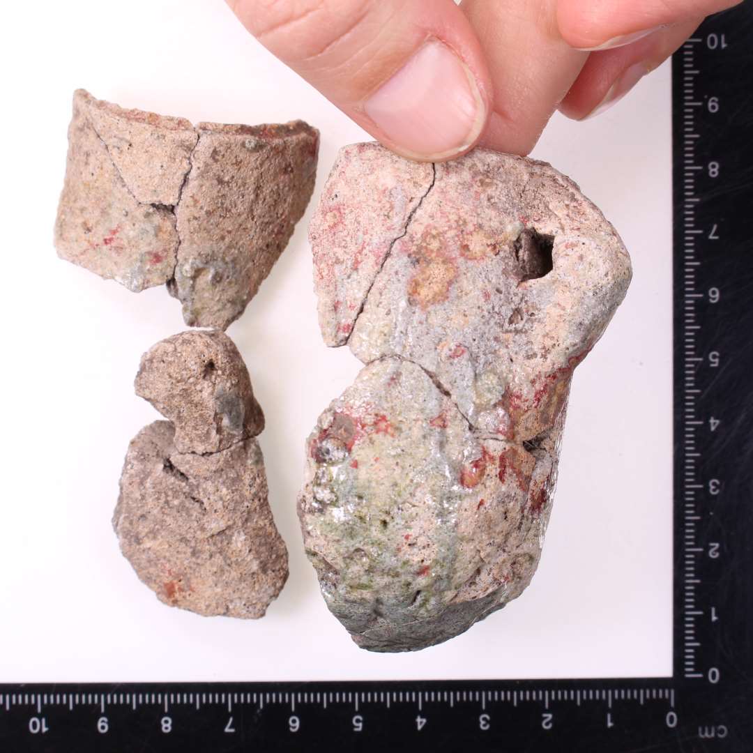 Digelsk�r
Samlet til fire fragmenter af samme digle, bl.a. komplet profil: ca. 7 cm h�j, og 4 cm i diameter. To lodretstillede �rer med vandret hul.