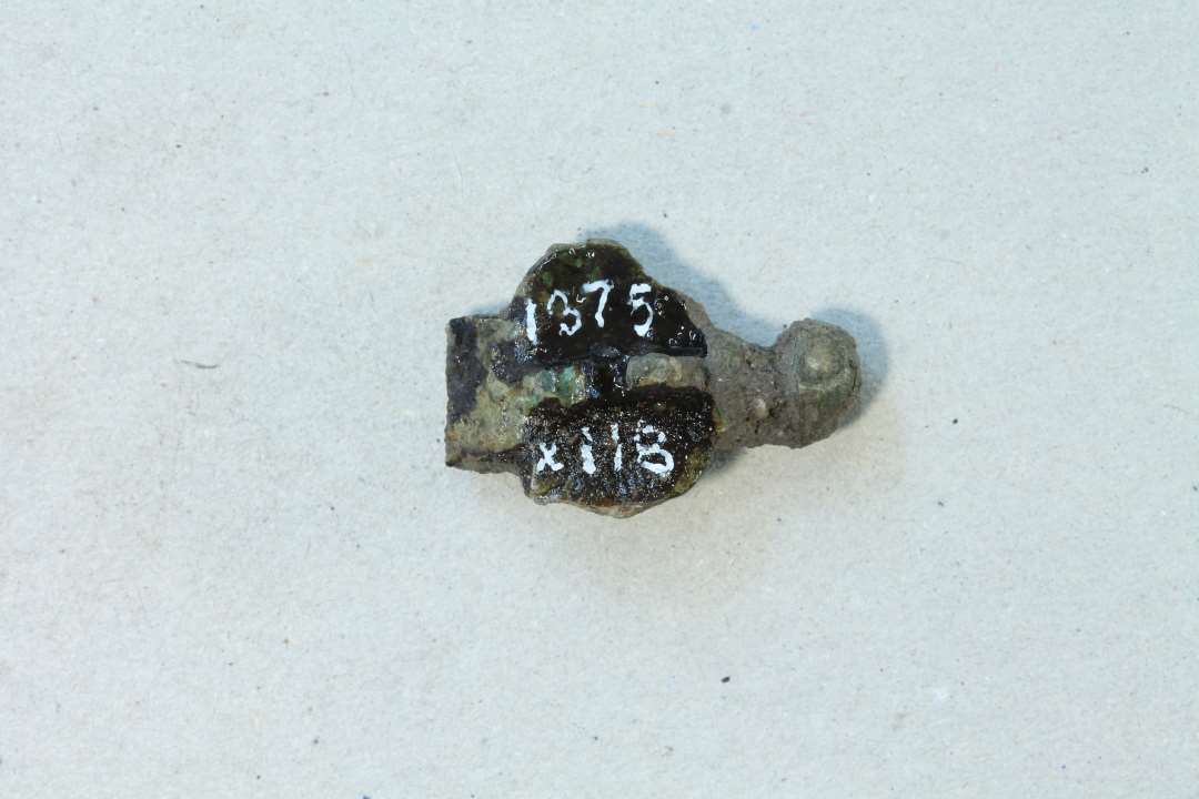 Hovedpladen af korsformet fibel. P� undersiden rester af enkelt n�lef�ste. St�rste m�l: 2,3 cm.