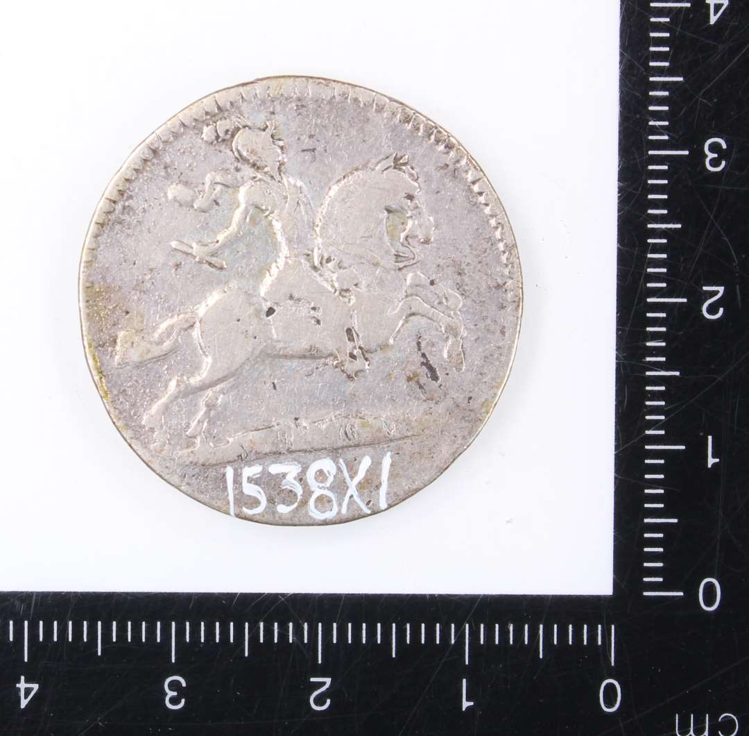 S�lvm�nt
En kopi af en guldm�nt, pr�get i Chr. D V`s tid. 
P� m�ntens forside ses en rytter med en depeche i h�nden. P� bagside er  tre C�r flettet ind i hinanden og i �bningerne i det herved opst�ede m�nster er indflettet romertallet V. Kanten er p� begge side riflet.��
M�ntens diameter 3 cm.�        
Tykkelse 1 mm.��
V�gt: 11,46 g.