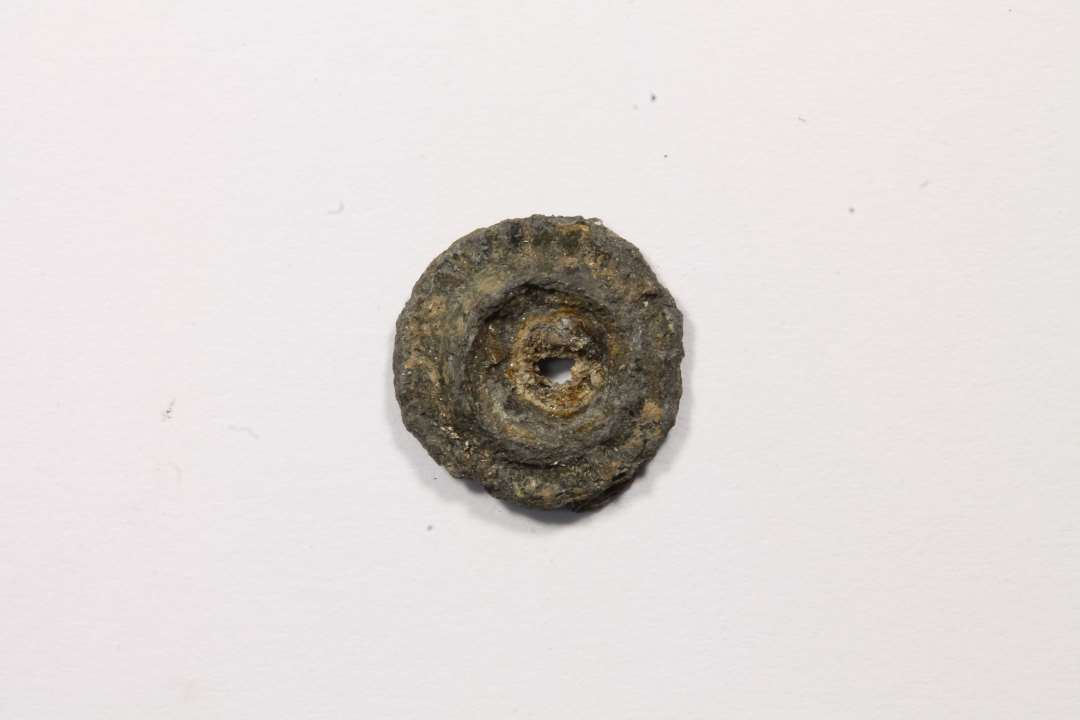 Mindre cirklul�r (9 mm) genstand med hul. Muligvis del af pyntenitte.  