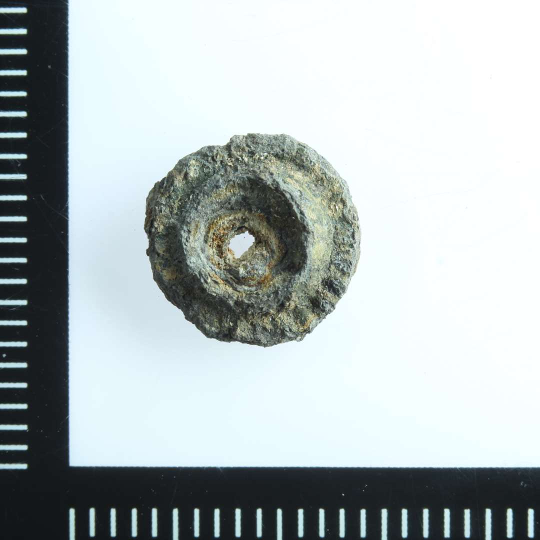 Mindre cirklul�r (9 mm) genstand med hul. Muligvis del af pyntenitte.  