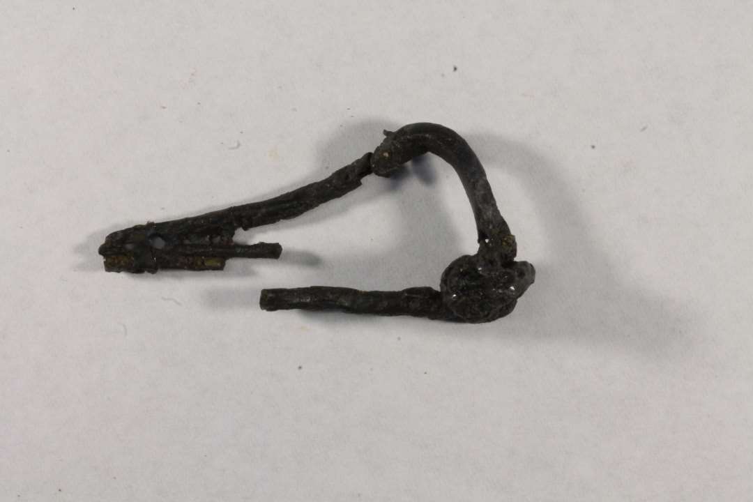 1 Jernfibel. 6,5 cm lang svajet fibel af sen-latene-skema med ydre tv�rtr�d og fire gennemboringer af n�leholderen. Spiralen er 1,7 cm lang og har 4 vindinger.�  Fiblen tilh�rer Kostrzewski type M.
