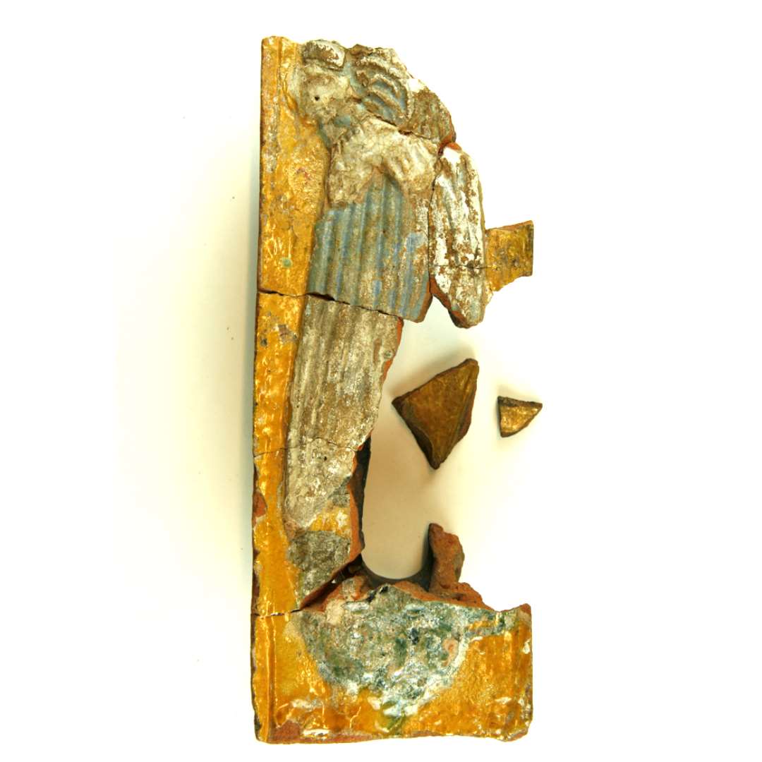 Fragment af polykrom, lodret listekakkel. P� en konsol st�r en unavngiven kvindeskikkelse if�rt fodsid, plisseret kjole med lange, vide �rmer med plisserede �rmegab og plisseret underbluse. Om halsen h�nger en sv�r guldk�de. H�ret er holdt sammen med et net, og p� hovedet har hun en baret smykket med de samme blade og den hvide blomst som p� de rektangul�re kakler, hvilket tyder p� at de er fra samme ovn. St�rste m�l: 23 cm. Sammenlimet af D1576, D1601, D1612. 