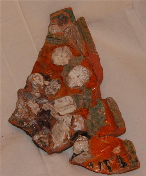 Fragment af polykrom kakkel. �vre venstre trediedel mangler. Sammenlimet af 8 stykker. I midten Kristusfigur med str�leglorie, brunt h�r og sk�g, med l�s brun kappe, med stav (korsfane?) i h�jre h�nd og med sin venstre st�ttende p� hovedet af liggende skelet. Bag hem en kiste. Han st�r p� liggende mandsfigur med lang brun kappe og brun hue. Langs rammen bugtede st�ngler med gr�nne blade og hvide blomster. I hj�rnet pappeg�je. P� et postament forneden indskriften: 'ann (0-1) ii -' med gotiske bogstaver, brune. Uprofileret ramme.�Oprindelig bredde: 18,8 cm. L�ngde: 25,8 cm.