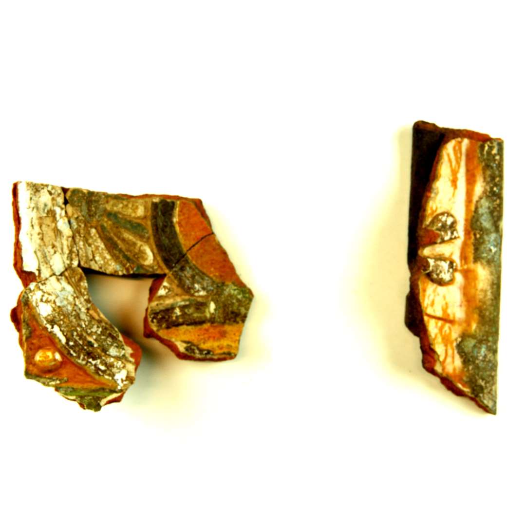 Fragment af polykrom kakkel, dekoreret som foreg�ende. Kapit�l af s�jle med bueslag til 2 sider. Over den h�jre roset med oval midte og skiftevis bl� og hvide kronblade. H�rer sammen med D1594 og sammenlimet med D1592 (1 stk.).