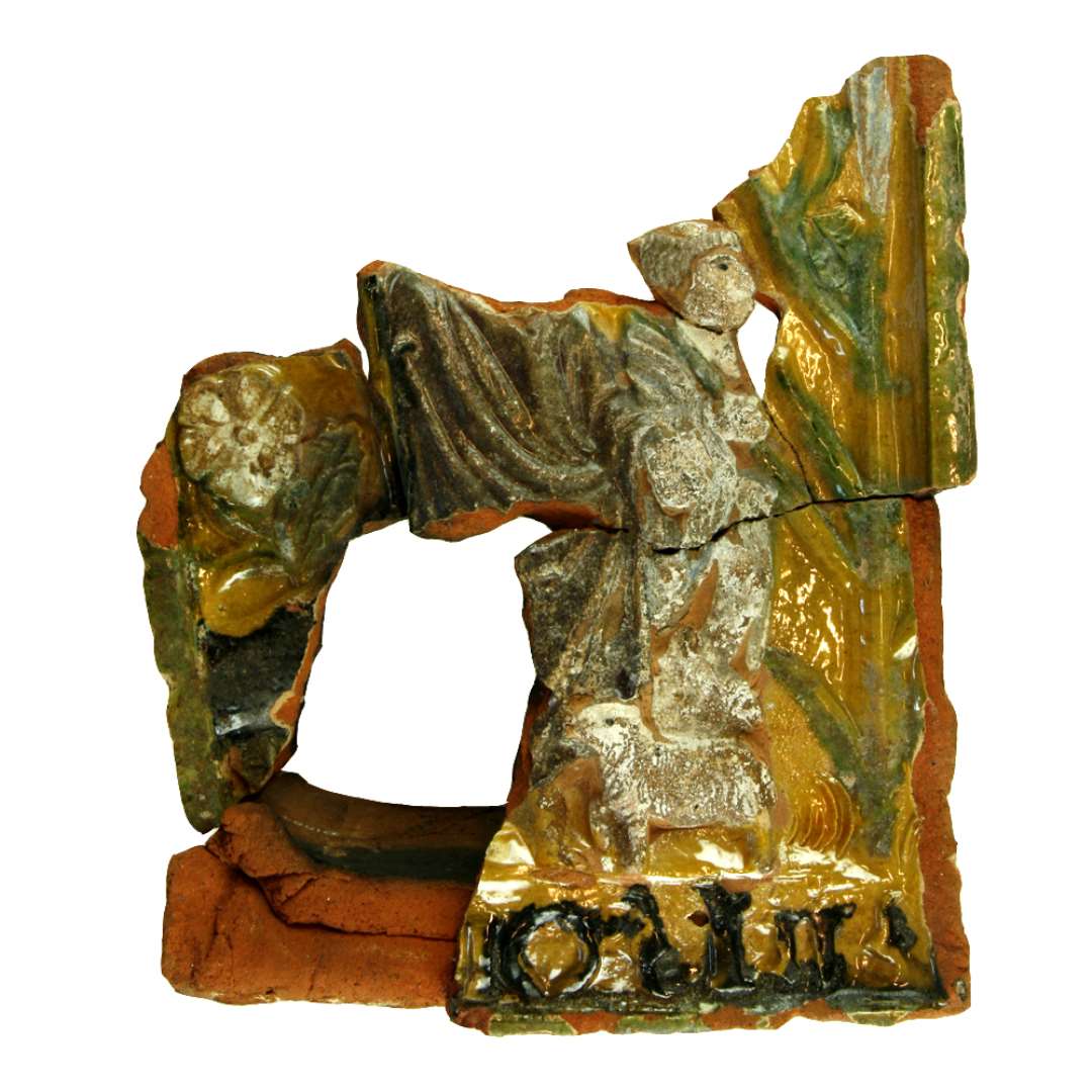 Fragment af polykrom kakkel. Motiv: Kristus med gul cirkelglorie, brun kjortel, bare f�dder. I h�jre h�nd holder han en hyrdestav (symbol p� sejrsfanen). Med den forsvarer han f�rene mod den sorte ulv, der kommer ind fra venstre. Med sin venstre h�nd viser Kristus ned mod to sm� hvide lam, menigheden, ved sine f�dder. til h�jre forsvinder levebr�dspr�sten med hyrdestav over skulderen. Sammenh�rende/sammenlimet med D1584, D1610, D1619. P� postament f�lgende indskrift i sort: '--- o - lii-' . St�rste m�l: 21,5 cm.