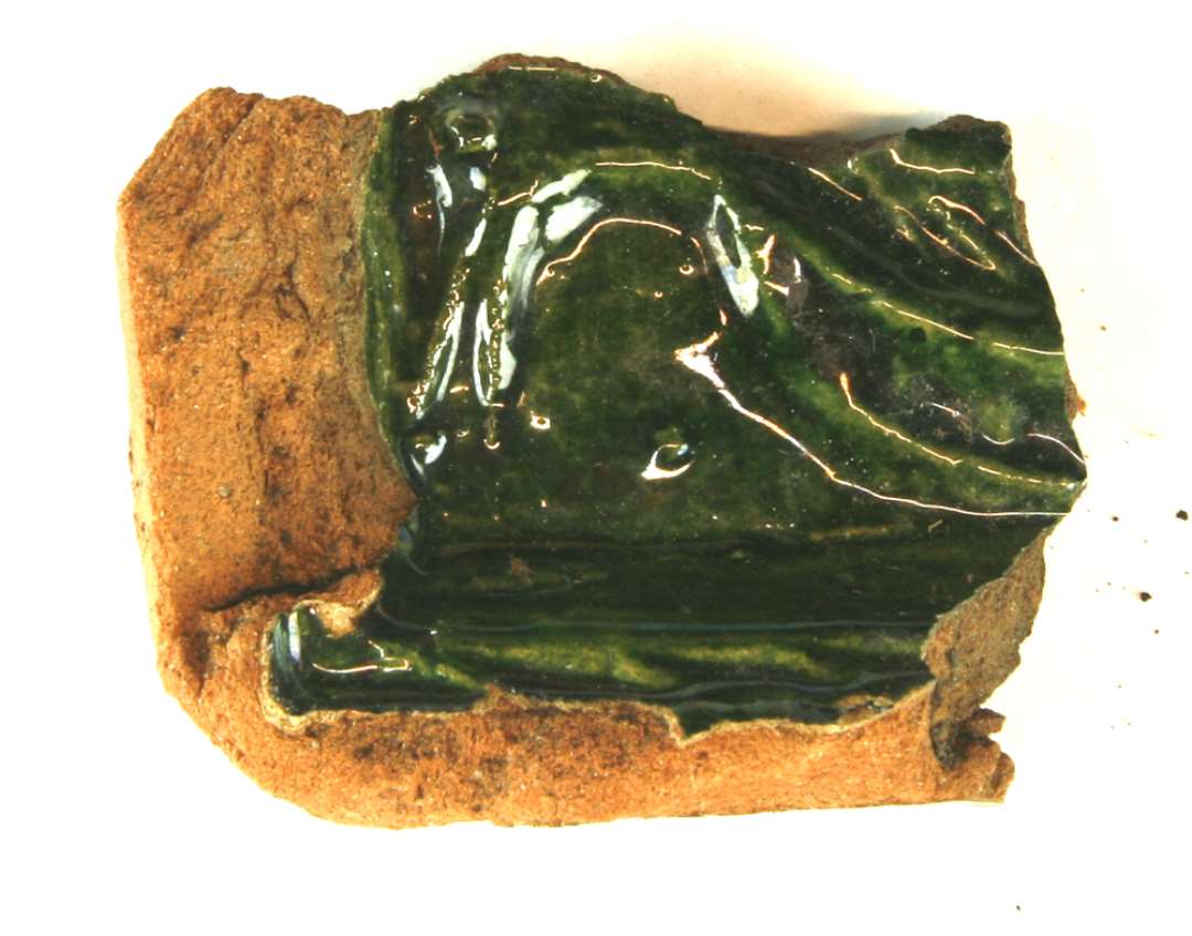 1 hj�rnefragment af r�dbr�ndt rumpekakkel med rest af reliefdekoration forestillende en fugl, p� bladet. Ydersiden pibelersd�kket og med gr�n blyglasur. St�rste m�l: 7 cm.