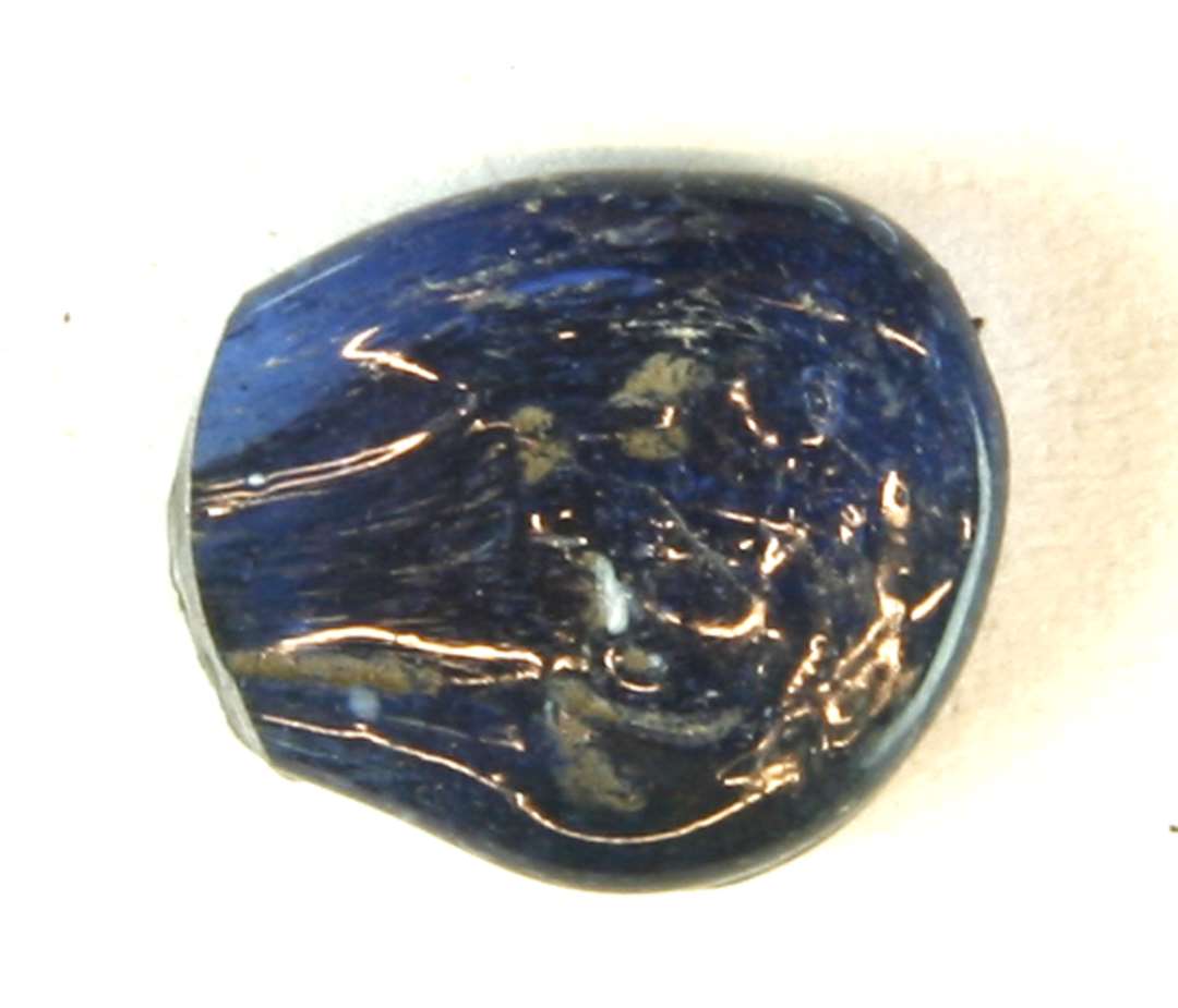 1 fragment af klart, bl�t gennemskinneligt glas, uden spor af nedbrydning. Stykket har form som en fladt udpresset dr�be og stammer fra enden af et stykke r�glas, som det fandtes ved vikingetidsgravningerne i Sct. Nicolajgade. Muligvis er der spor af en tang i overfladen.�St. m�l: 1,5 x 1,3 cm. Tykkelse: o,4 cm.