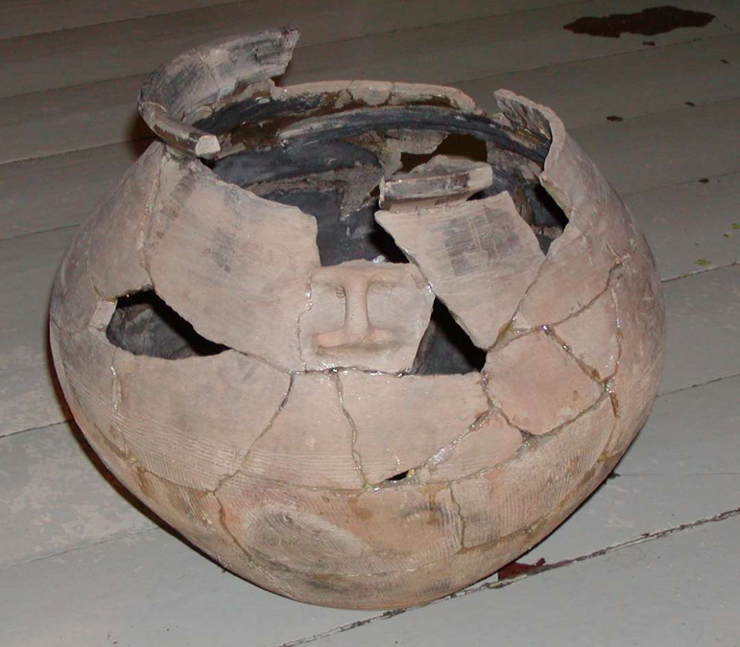 1 n�sten komplet urne, samlet af mange sk�r. 29 cm h�j, randen ca. 22 cm i diam., st�rste bugdiam. ca. 32 cm. P� overdelen et st�rkt x-formet  (pynte-)�re, ellers ornamenteret med tre vandrette furer der afsluttes p�nt ved �ret. Randen kraftig faceteret.  Karets underdel ornamenteret med kamfurer, foroven afsluttet vandret, ellers lodret afstribning bortset fra fire partier, hvor kamfurerne er lodret b�lgede.