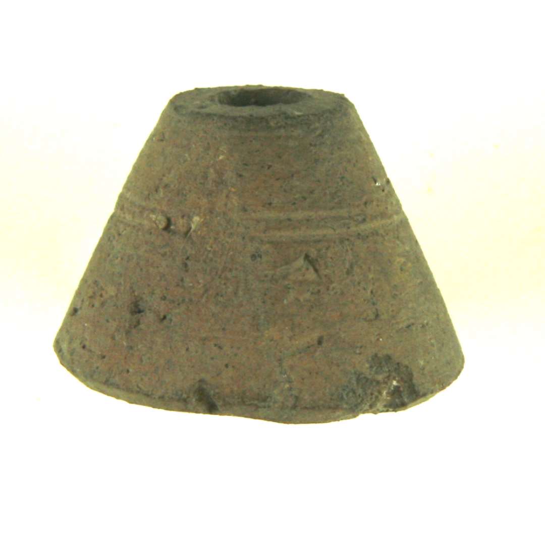 Tenv�gt af brunbr�ndt ler. Konisk form, drejet arbejde med bunden afsk�ret med kniv. Om siden en oml�bende dobbeltfure. H�jde: 2,7 cm. Diameter: 3,6 cm.