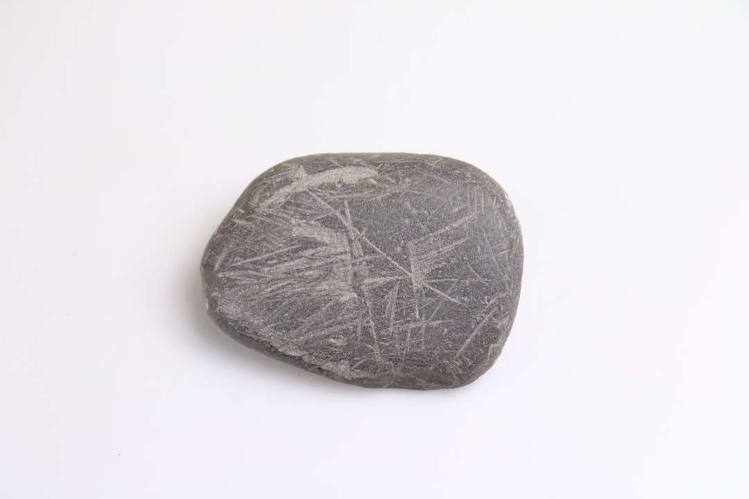 1 sort  flad, rund sten med mange indridsede furer evt, n�leglatter. St�rste m�l: 9,5 cm.
