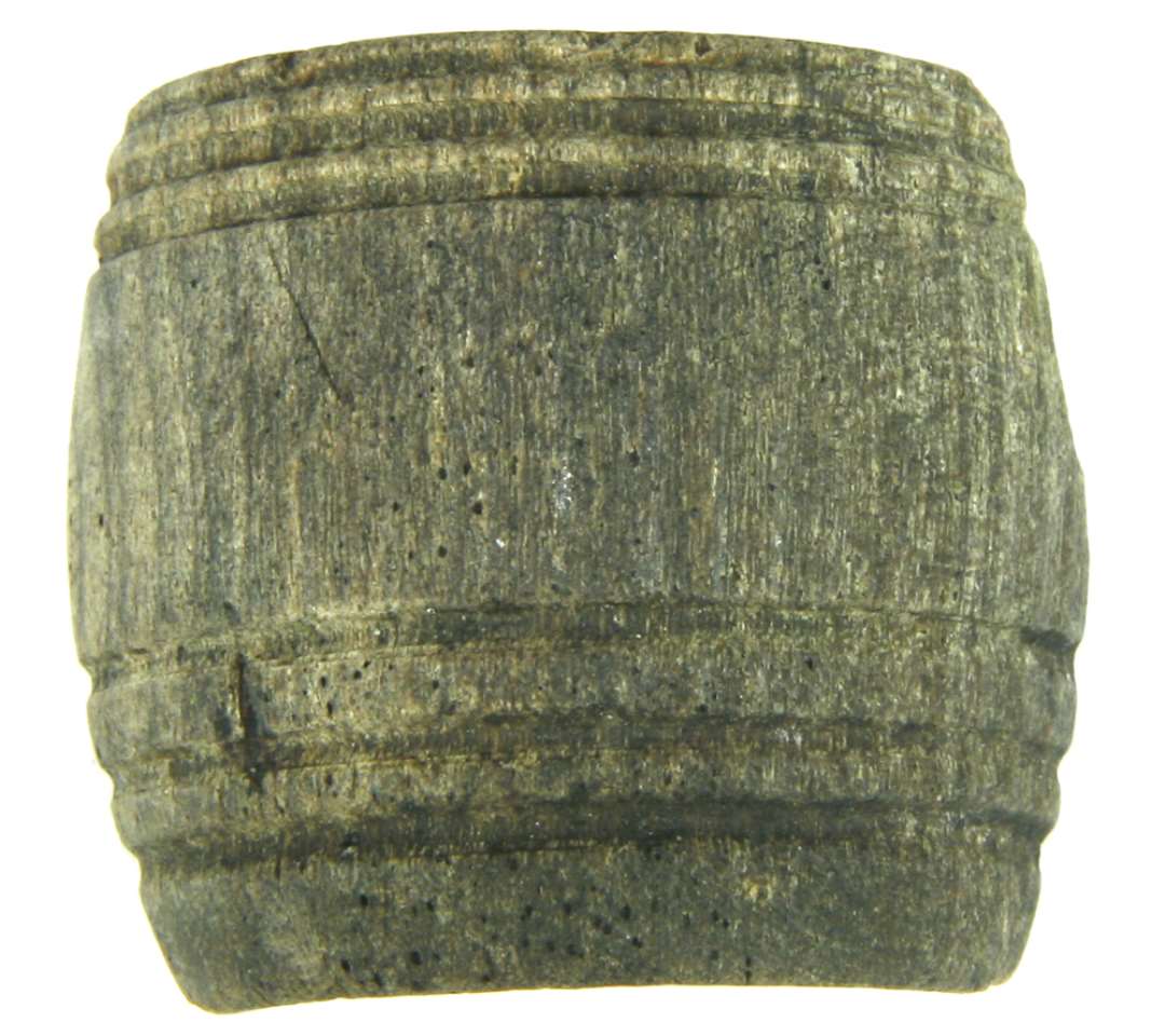 Fragment af drejet ganske lille tr�beholder af let dobbelt konisk form og af en vis lighed med en miniaturet�nde, hvoraf knap halvdelen er bevaret. Beholderen har udvendig plan med en skarprygget fodrand ca. 1,5 mm h�j. Ca. 0,5 cm. fra fodranden findes p� beholderens side en 0,8 cm. b�lte med tre ca. 1,5 mm brede og dybe inddrejede furer med rund bund og to mellemliggende flade vulster. Umiddelbar under mundingsranden findes et ca. 0,6 cm. bredt b�lte ligeledes med tre dybt inddrejede furer og to smalle vulster, idet den �verste af vulsterne er plaseret ganske t�t ved mundingsranden, kommer denne til af fremtr�de med l�berand. �P� beholderens inderside er der i ca. 0,5 cm. bredde under mundingsranden inddrejet et skruegevind til l�g. Beholdernes indre er formet som et hulrum af fladtrykt kugleform med en bundtykkelse p� 0,7 cm. og et sidestykke p� ca. 0,25 cm.�Beholderens h�jde: 3,4 cm. Fodrandens diameter: 3,2 cm. Mundingsdiameter: 3,5 cm. Midterdiameter: 3,85 cm.