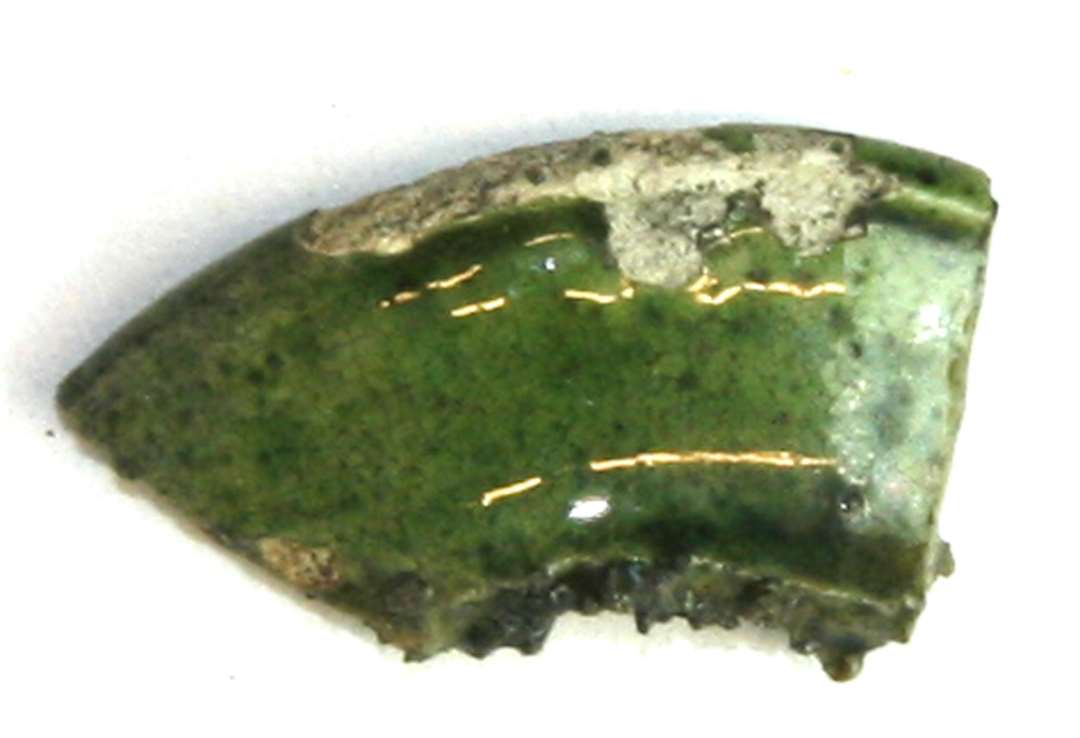 Randsk�r af bred, flad kraveform af meget tyndt gods, gr�lig h�rdtbr�ndt pibelersmasse med gr�n, til dels afskallet blyglasur p� inder- og ydersiden. Fra miniaturekrukke.