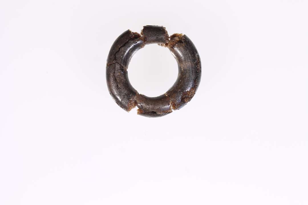 To glasringe. Den ene, sammenlimet af fire stykker, er af nu mat, gr�sort, uigennemsigtigt glas, 1,8-1,85 cm i diam., udf�rt af en ca 0,45 cm tyk p�lseformet glastr�d, der p� ringens sammenf�jningssted kun andrager godt 0,3 cm. Den anden af st�rkt uregelm�ssig cirkelform er af blankt gyldenbrunt nu uigennemsigtigt glas, fra 1,5-1,6 cm i diam. Ringp�lsens tykkelse varierer fra knap 0,3 cm til 0,2 cm p� sammenf�jningsstedet.