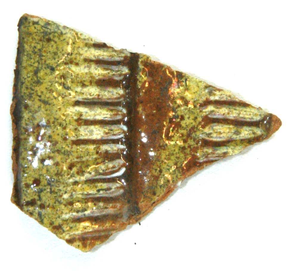 Skuldersk�r af r�dbr�ndt lergods, p� ydersiden forsynet med vandratte fremspringende b�lter, aftappet over hinanden; under hvert fremspring indpressede r�kker af lodrette streger, i �vrigt pibelersbegitning, hvorover klar blyglasur.