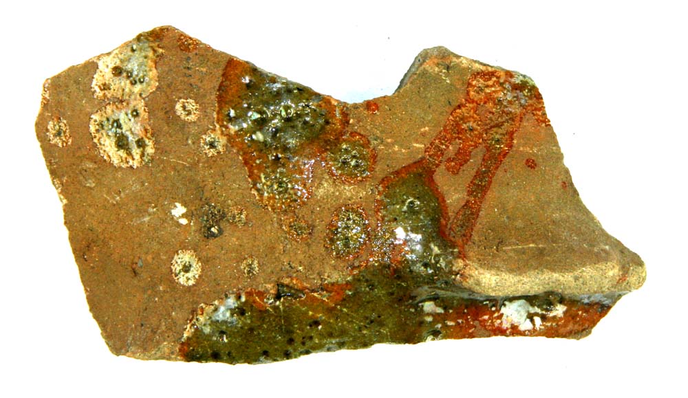 Bundsk�r af gr�brunt lergods fra kar, hvis fodparti med ca 4 cm's mellemrum har v�ret forsynet med udtungede, brede svagt fremspringende f�der. P� ydersiden pletvis anbragt gr�nlig blyglasur.