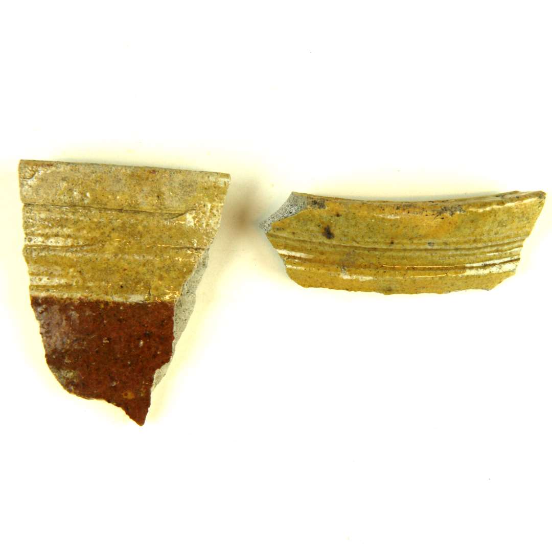 To randsk�r fra kander af gr�ligt, pibelersagtigt gods. Sk�rene har let indadskr�nende mundingsrandsoverside med fremst�ende skarpkantet l�berand, medens halspartiet udviser skarpryggede vulster og furer. Det ene sk�r udviser ca 2,5 cm under mundingsranden en begitning af r�dler. Overfladen p� begge sk�r er d�kket af klar blyglasur.