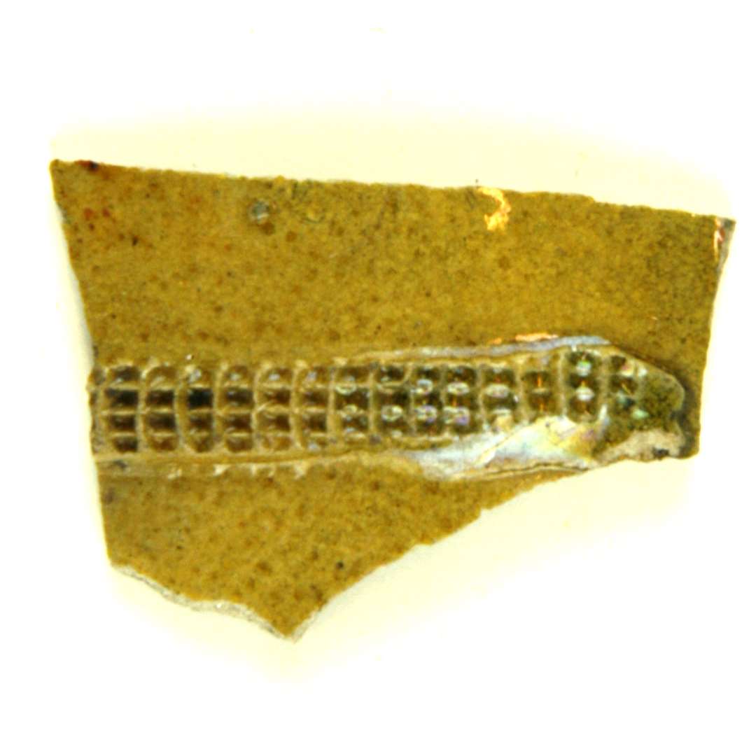 Bugsk�r af gr�ligt, pibelersagtigt gods, p� ydersiden forsynet med p�lagt b�nd af samme gods, hvori er indstemplet t�t anbragte millimeterstore rektangler i regelm�ssige r�kker. Hele overfladen d�kket af klar til let gr�nlig blyglasur.