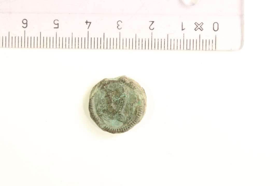 1 skiveformet bronzepatrice ?, 1,8 x 0,4 cm.�Den ene side med markant perle-kant, samten flade d�kket med tre stiliserede fuglehoveder, delvist sammenh�ngende i trekantform.�Datering: YGJ