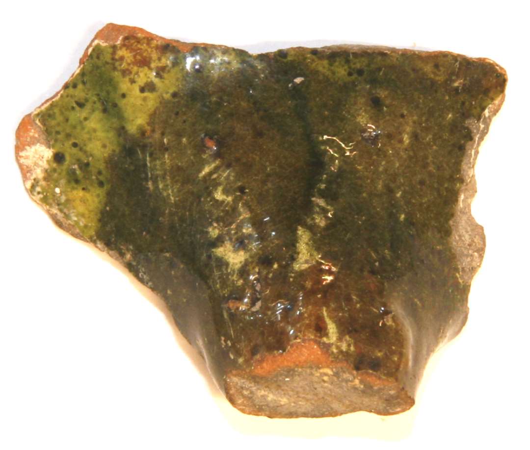 Sidesk�r med basisparti af rund trind hank fra kande. Medens sk�rvens k�rne er sortbr�ndt er indersiden dybr�d og ydersiden belagt med pibeler d�kket af dybgr�n blyglasur.