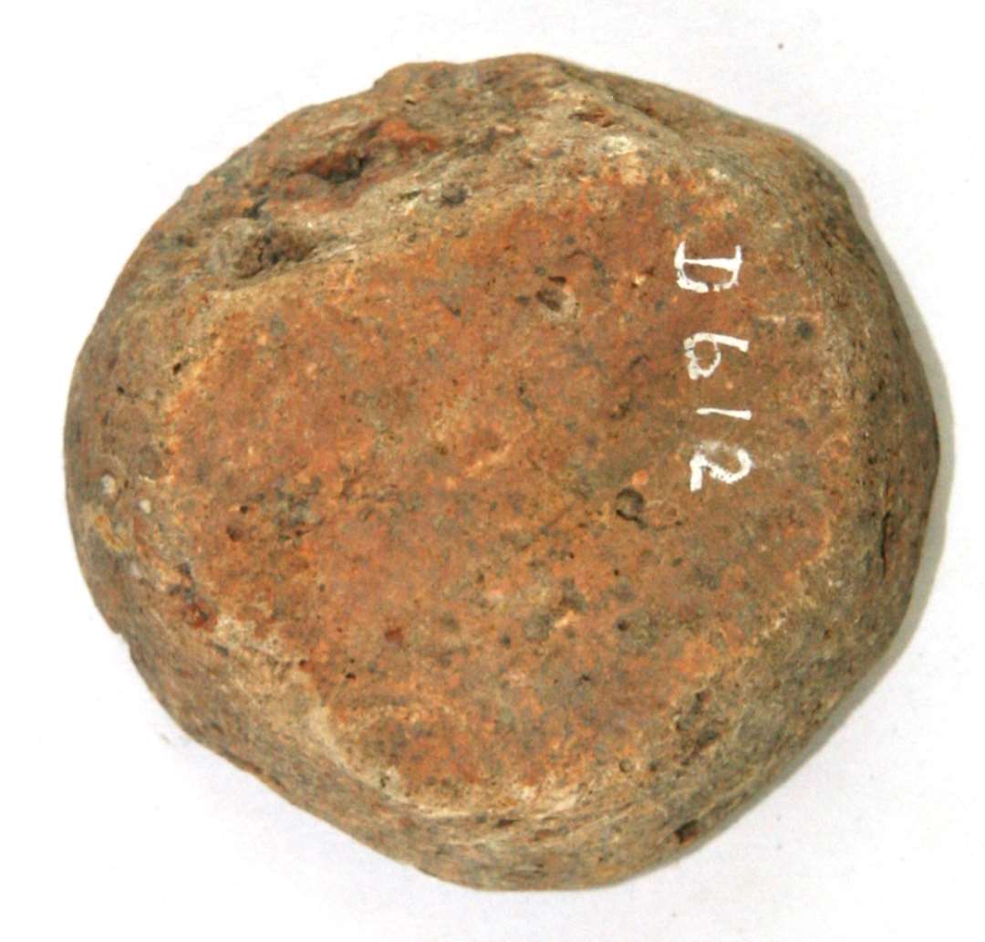 Skive af gulgr�t br�ndt ler, uregelm�ssig cirkelrund form med skr� sider, idet den ene fladside m�ler 5,5 - 6 cm. i diameter, den anden kun 0,5 cm. Skiven synes formet ved tilhugning og efterf�lgende slibning og afrunding efter br�ndingen.