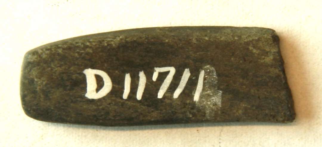 1 miniatureslibesten af gr� sandsten af tynd, flad stangform, nedslebet p� midten, hvor stykket er overbrudt. L: 3,4 cm. Br: 1,2 cm. St. tyk: 0,55 cm.