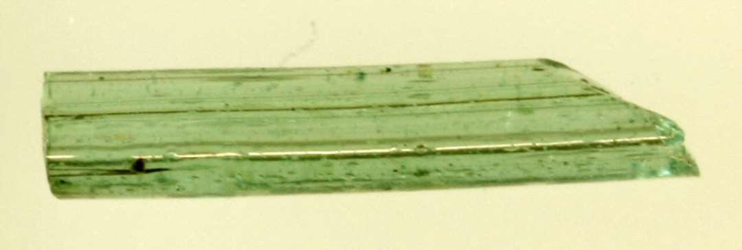 1 glasstang af oval tv�rsnitsform, overbrudt i begge ender, af gr�nligt, gennemsigtigt glas. L: 2,0 cm.