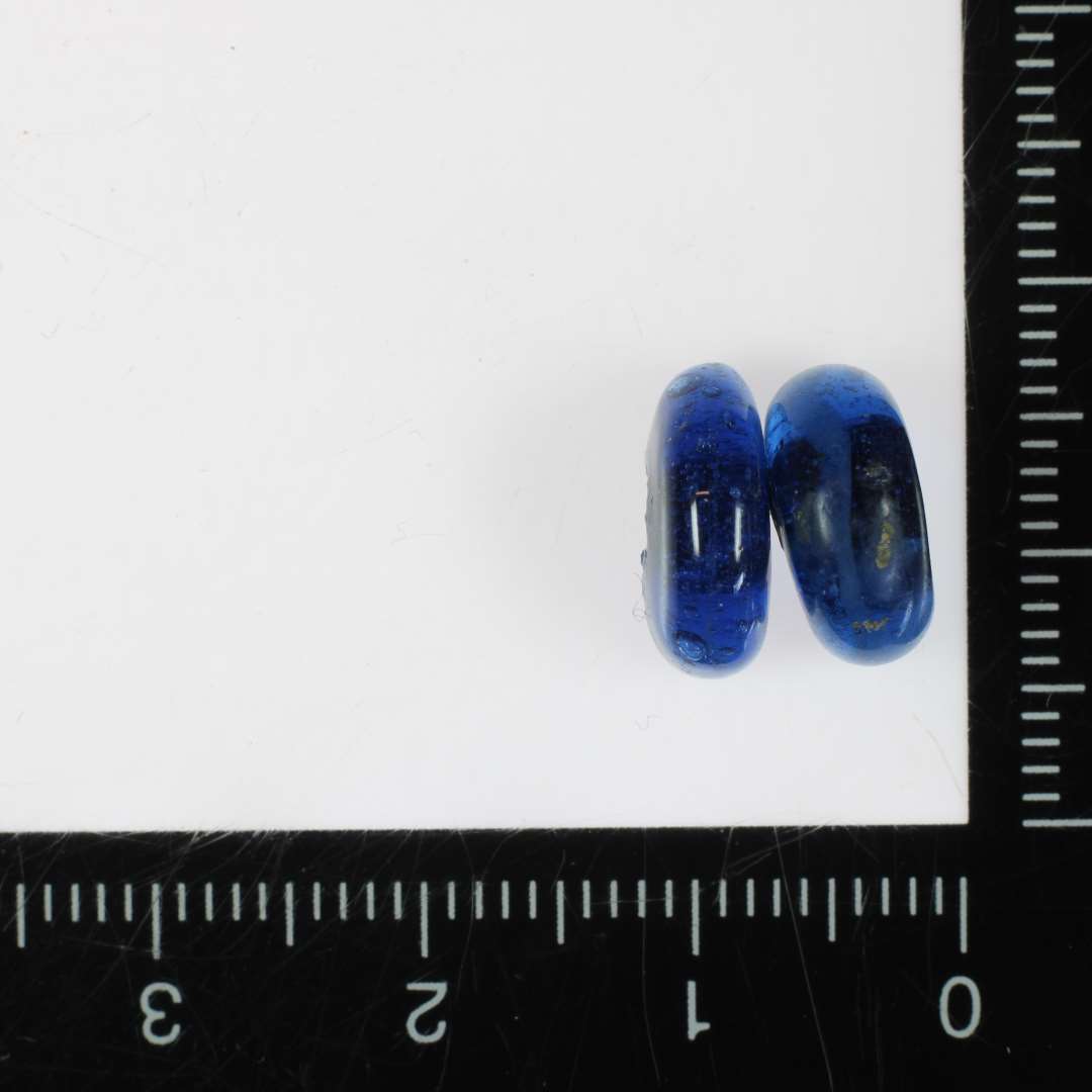 2 halve perler (ikke samh�rende) af afrundet ringform og af bl�ligt gennemsigtigt glas. a: 11 mm., b: 11 mm.