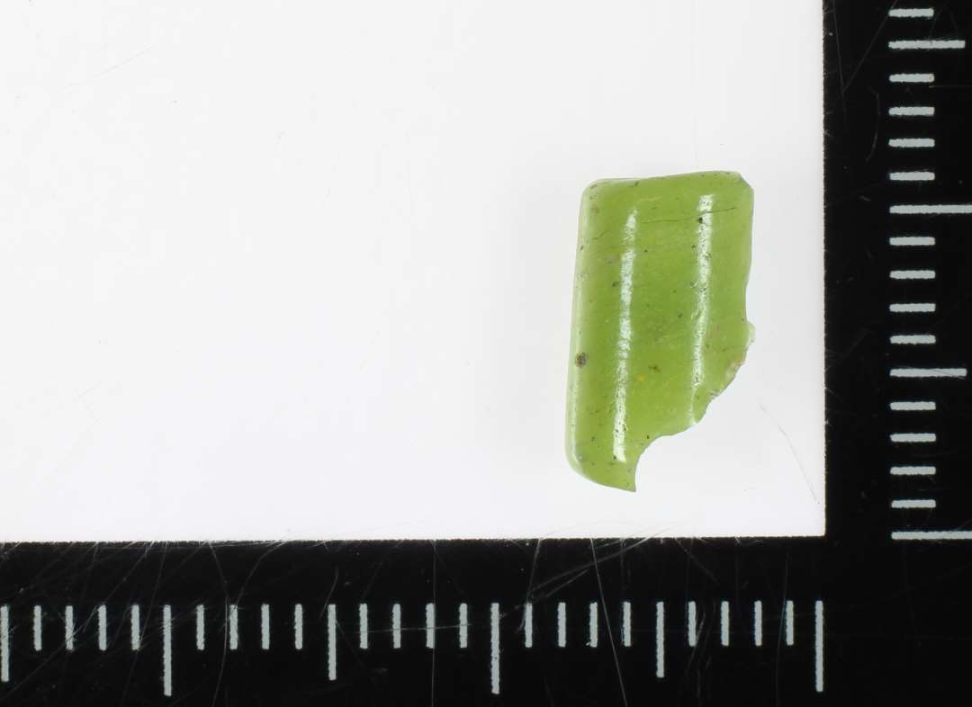 1 fragment af perle af aflang cylinderform spaltet p� langs af bleggr�n ugennemsigtig glasmasse. 10 mm.