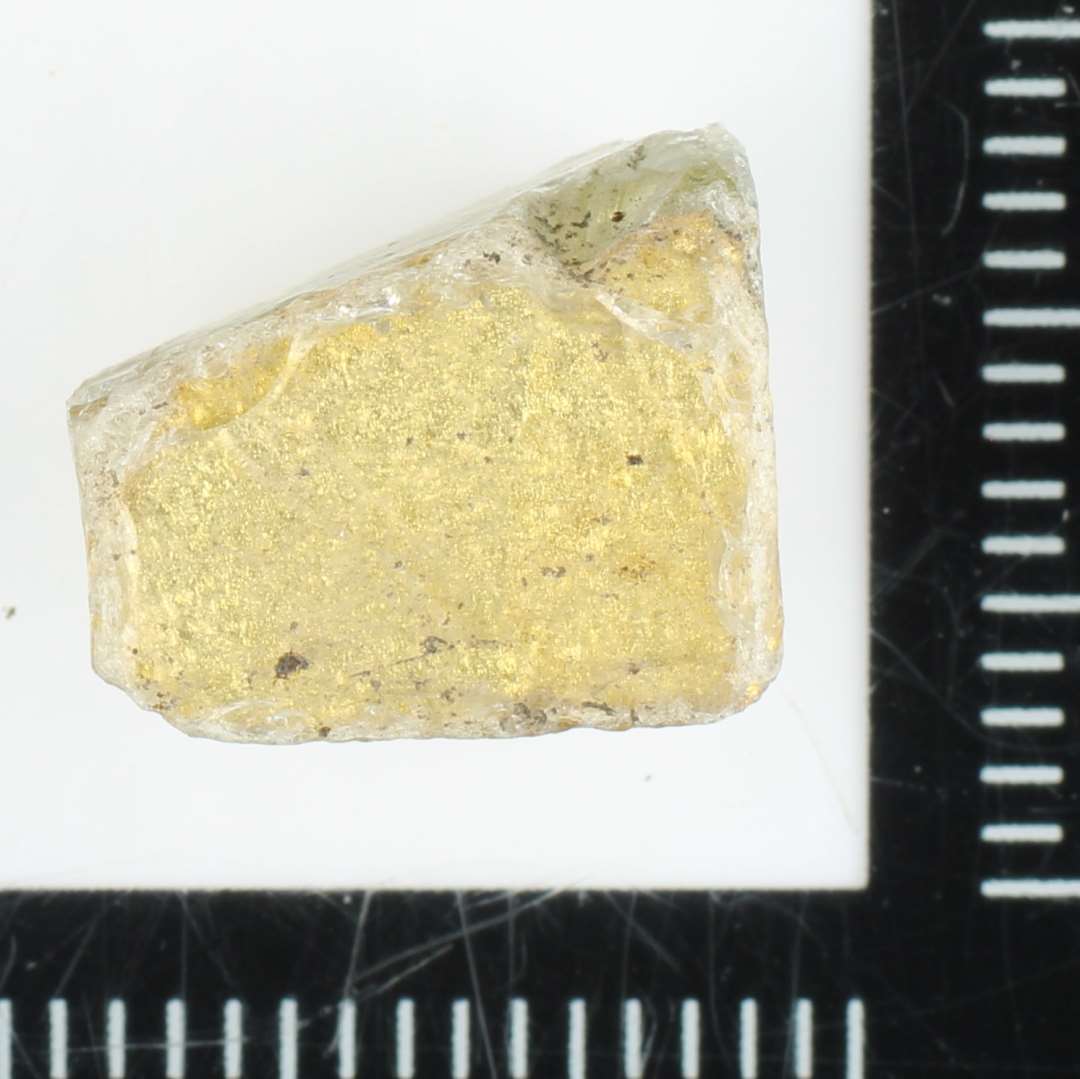 1 fragmenteret mosaikstift af klart gennemsigtigt glas med indlagt guldfolie p� den ene sideflade.