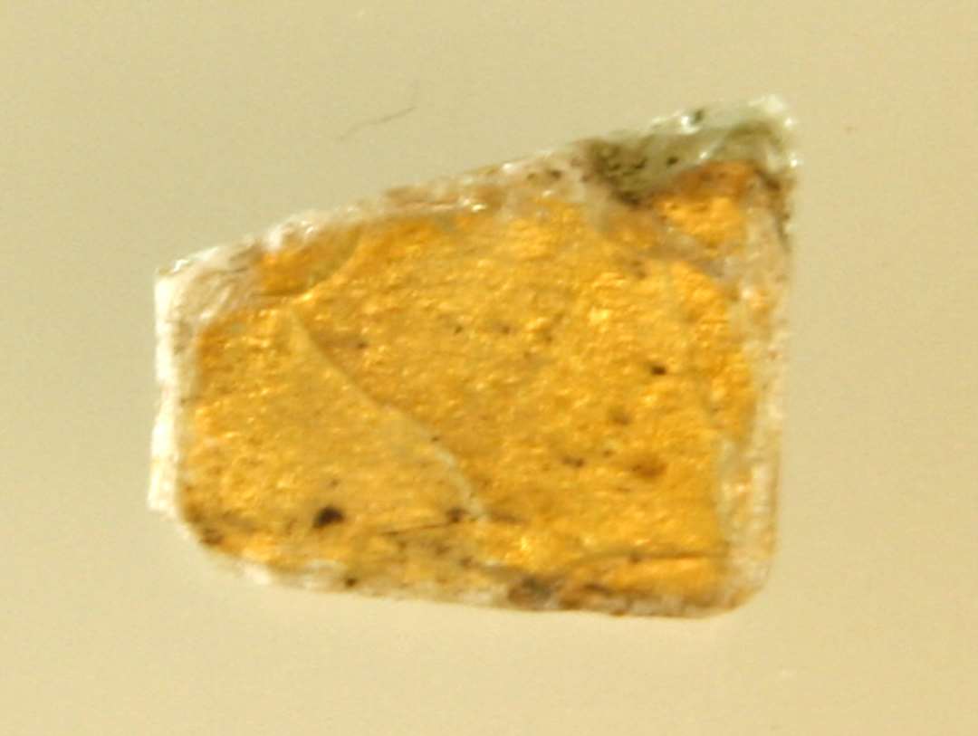 1 fragmenteret mosaikstift af klart gennemsigtigt glas med indlagt guldfolie p� den ene sideflade.