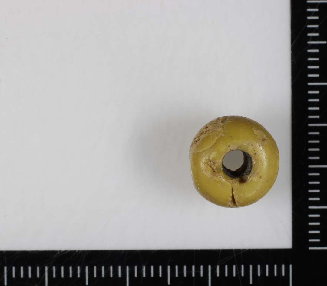 1 perle af sk�v fladtykt kugleform af gulligrumset ugennemsigtig glasmasse med luftgruber. 11 mm.