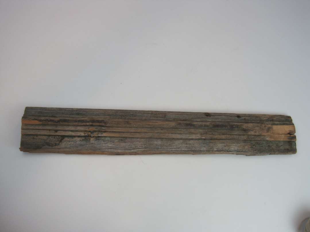 Udsavet stykke fyrretr�sbr�t med profilh�vlet forside. Dennes ene kant er afrundet og i tilknytning hertil er h�vlet et profil i form af to aftrappede platter og derp� en halvstaf. Spor efter bemaling.�M�l:�L�ngde: 60,5 cm.�Bredde: ca. 10 cm.