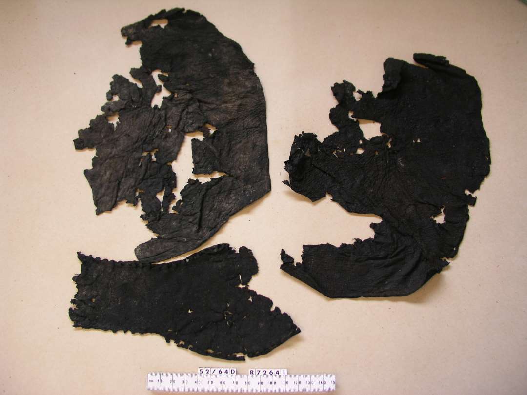 Bevaret l�der: Tre l�ders�ler: 1 S�l til h�jre Fod og 1 S�l til venstre fod (lidt beskadiget i Snuden) begge paa voksen Person. J�vnt afrundede Former med modereret Indknibning i Vristen. St�rste L�ngde henholdsvis: 26 cm og 23,7 cm. Barnes�l til venstre fod. J�vnt afrundet form med moderat Indknibning i Vristen. St�rste L�ngde ca. 12 cm. To sidekiler af sk�v Tragtform til sidesn�ret Sko af tyndt indt�rret S�der. Det ene har syv Sn�rehuller eller Spor af saadanne langs den ene Rand. St�rste M�l ca. 5,5 x 9 cm.�